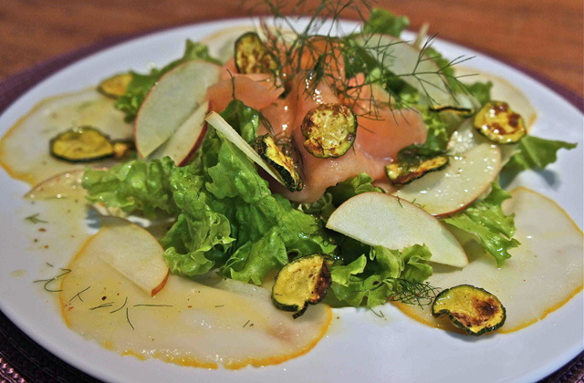 Foto de uma salada com folhas verdes, peixe defumado, maçã, abobrinha, molho de maracujá e funcho